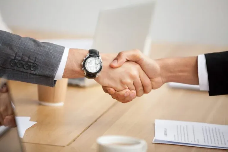 two business professionals shaking hands, symbolizing a coming to agreement on terms.